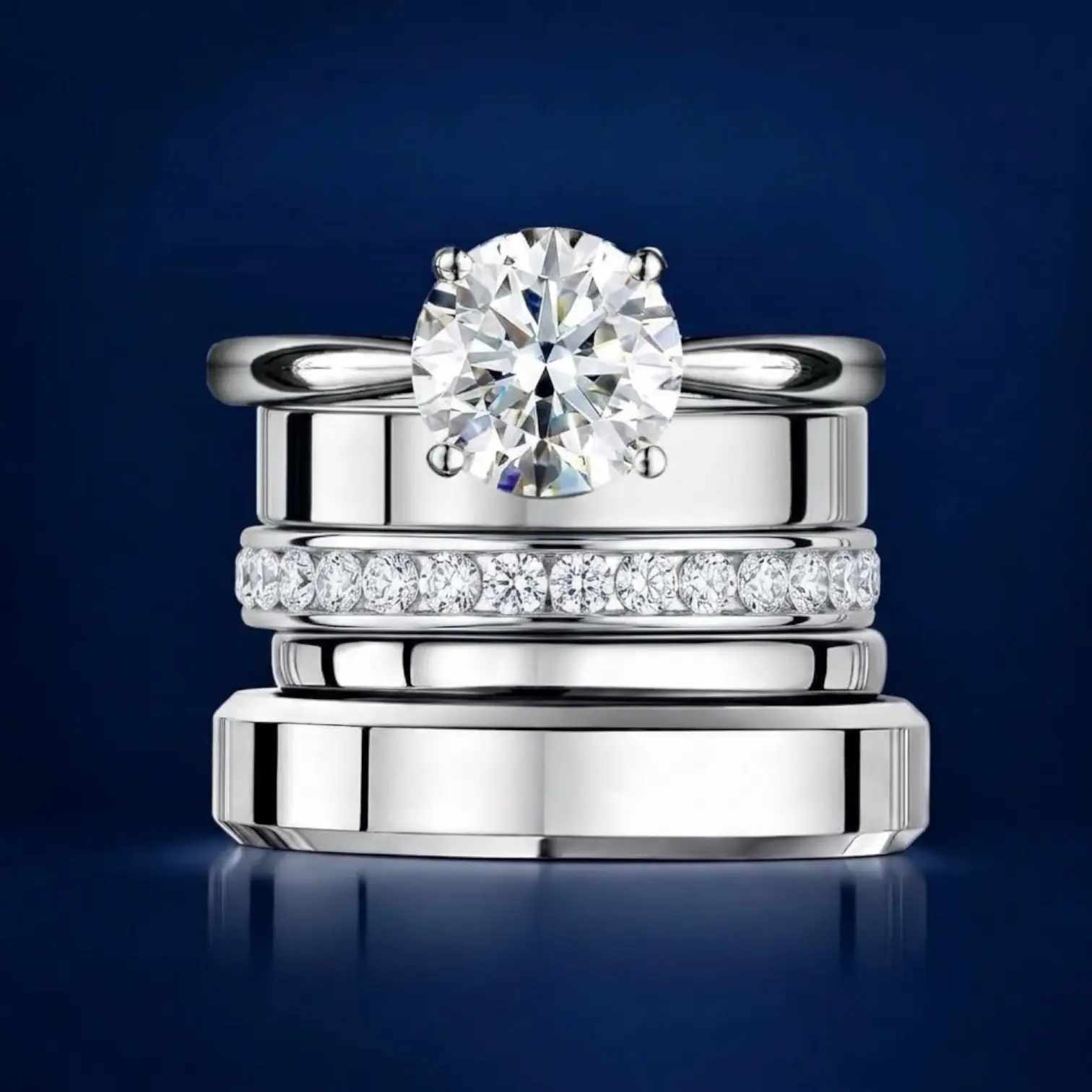 Platinum engagement ring, diamond ring and wedding rings arranged in a stack on a navy background