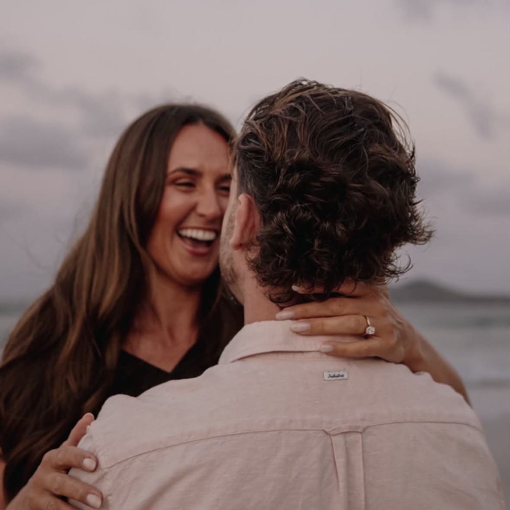 Sophie and Jordan kissing while celebrating their engagement by the sea