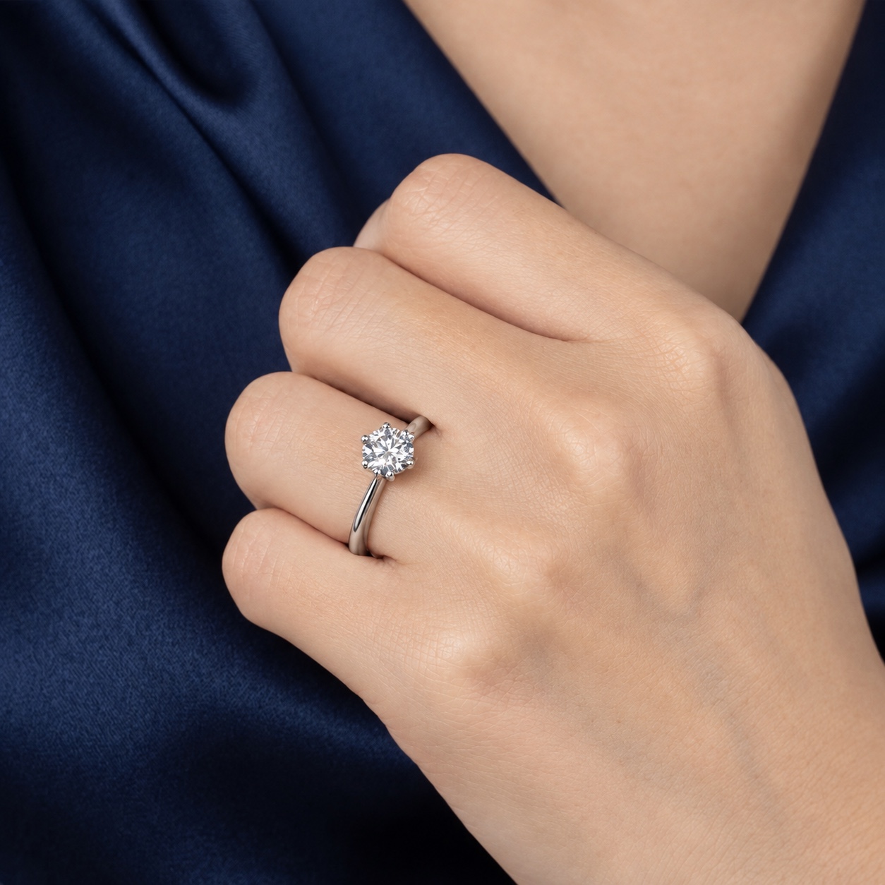Round brilliant cut diamond solitaire engagement ring worn with navy satin