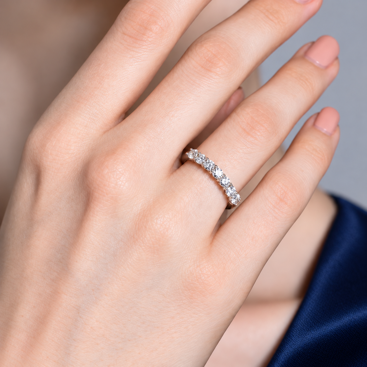 Seven stone diamond eternity ring worn on a hand with navy satin