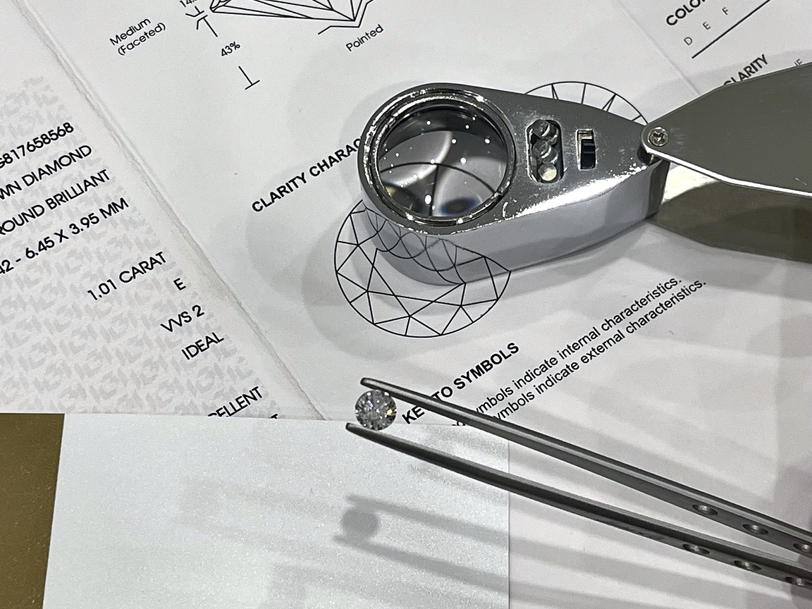 Loupe and a diamond held in tweezers above a grading report