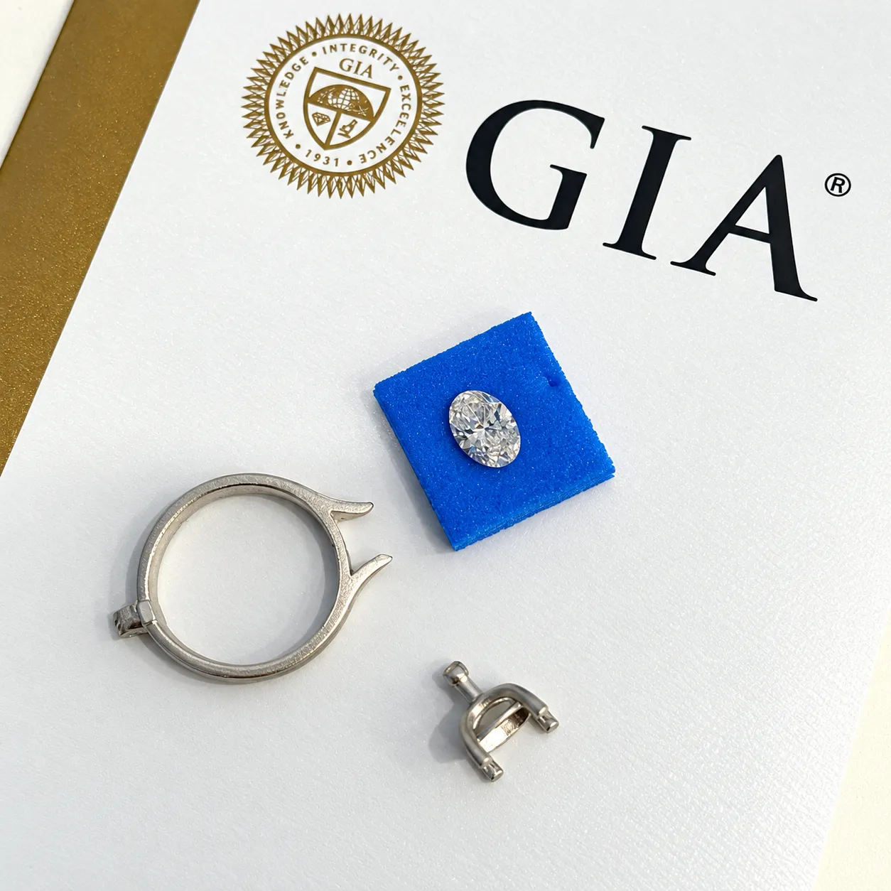 Loose GIA graded oval cut diamond beside the platinum ring components, photographed on a white GIA report.