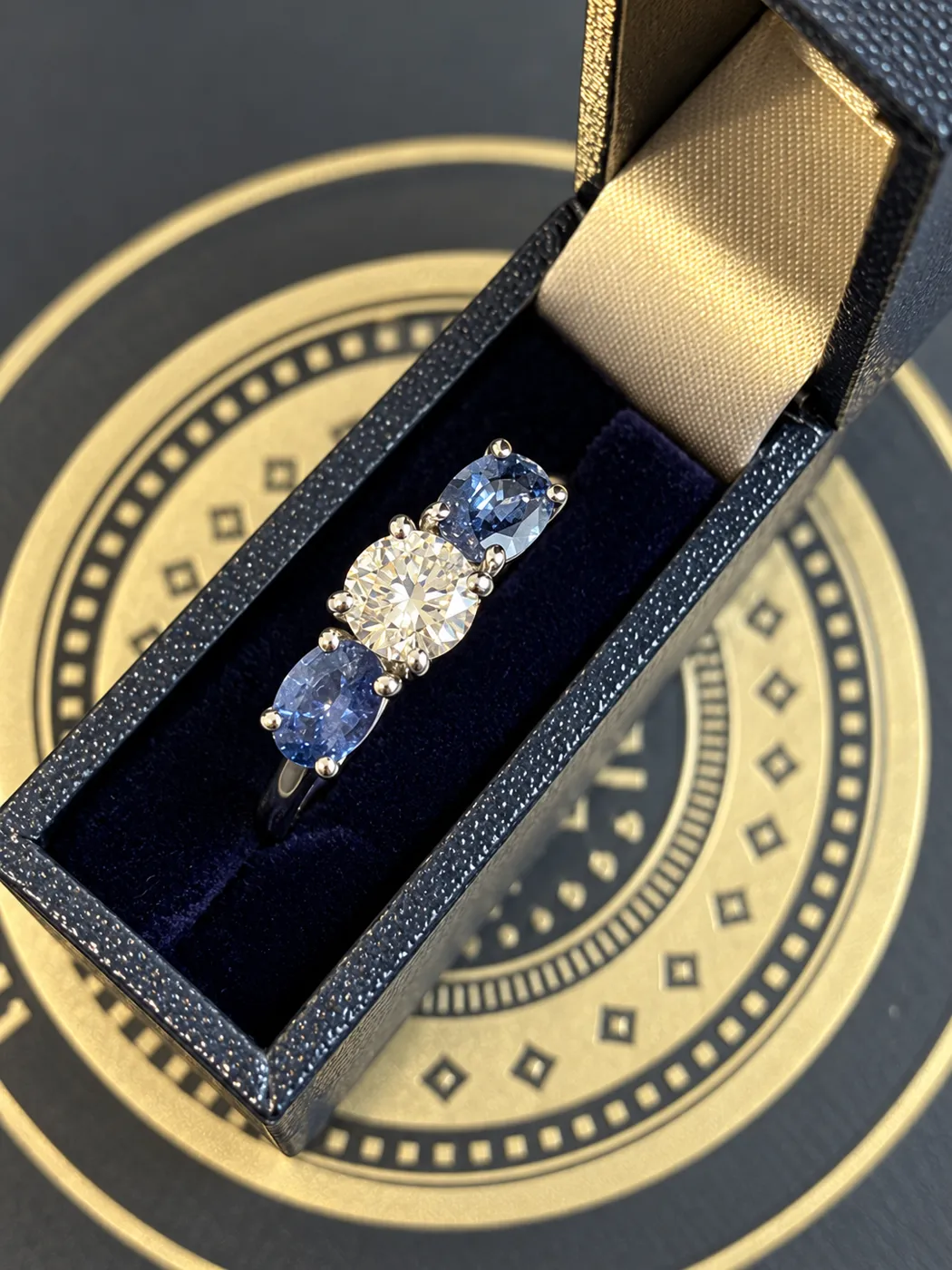 Finished platinum ring with a round brilliant cut diamond and two oval cut sapphires.